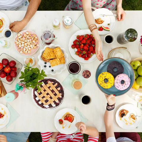 Top view of a colorful brunch table with fruit, pastries, and beverages, featuring donuts being offered on a blue plate.