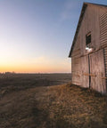 Beast Outdoor LED Barn Light For Dusk To Dawn Security illuminating a wooden barn at sunset with aluminum gray finish