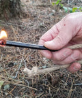 Hand using Ferro Rod Fire Starter Kit With A Large One Half Inch Rod, Fire Tinder And Custom Carry Pouch on forest floor
