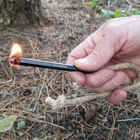 Hand using Ferro Rod Fire Starter Kit With A Large One Half Inch Rod, Fire Tinder And Custom Carry Pouch on forest floor