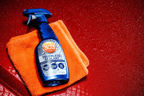 Touchless SiO2 Shield Sealant bottle on orange cloth, red glossy background, water beading effect, 1 gallon refill for trigger bottle