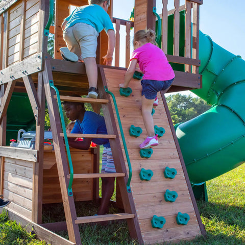 Children playing on Cedar Cove Wooden Swing Set With Spiral Tube Slide And Wave Slide, Elevated Clubhouse With Balcony