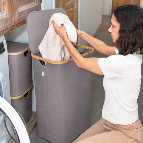 Woman using Breathable Fabric Laundry Hamper With Lid, Bamboo Frame, Side Handles, 26 Gallon Gray Go-To Laundry Basket in laundry room