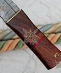 Close-up of Damascus Steel Fixed Blade Camping Knife with walnut handle and brass bolster, highlighting hand-forged detail.