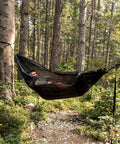 Person relaxing in Ultralight Pocket Hammock For Solo Adventures, supported by trees, in forest setting.
