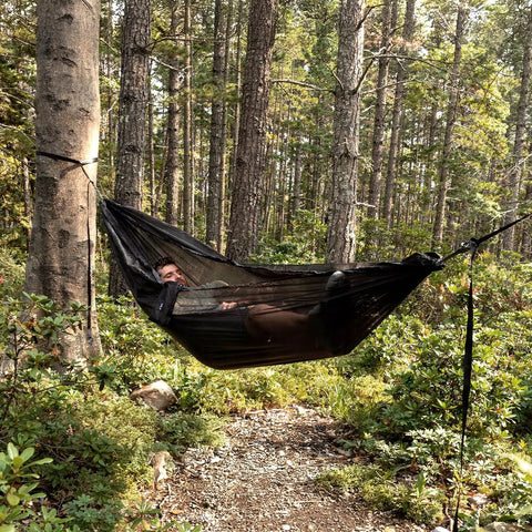 Person relaxing in Ultralight Pocket Hammock For Solo Adventures, supported by trees, in forest setting.