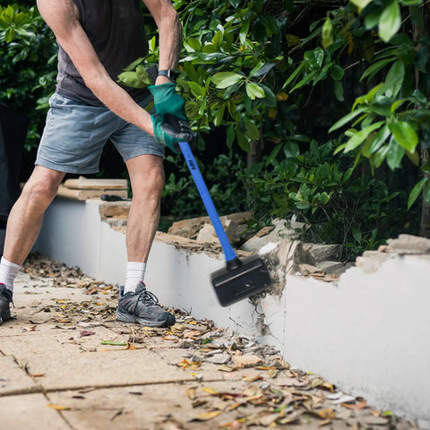 Person using 10 Lb Rubber Mallet Dead Blow Hammer For Woodworking And Automotive Use, 35 Inch Handle on garden wall.