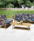 Outdoor wicker furniture with blue and green floral cushions on a patio, surrounded by green foliage.