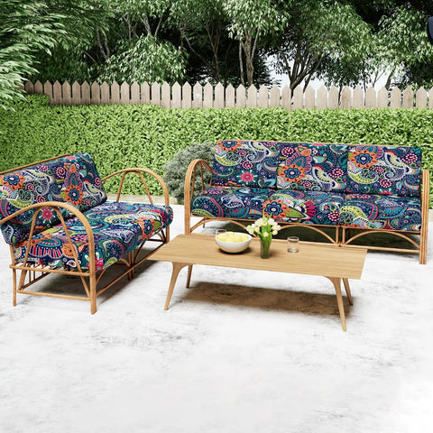 Outdoor wicker furniture with blue and green floral cushions on a patio, surrounded by green foliage.