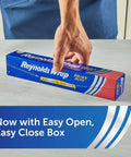 Person holding Heavy Duty Aluminum Foil Roll Beefy Strength 12 Inch Wide 50 Square Feet With Secure Easy Open Tab package on table