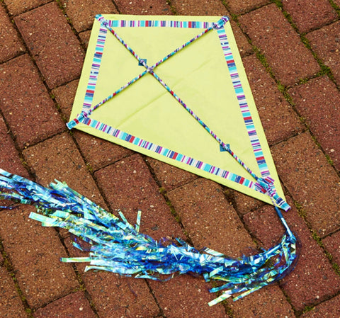 Yellow kite with striped border and blue tail on brick pavement.