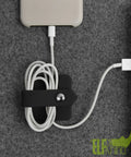 Headphone Case And Cable Organizer For Earbuds And Headphones Cord Winder And Earphone Holder Case Wrap Winder Headset Keeper Cable Manager Portable Silicone Black Cover in use organizing phone cable with snap closure on gray surface
