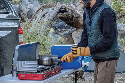 Person wearing Ranchworx Winter Work Gloves RWDI Premium Leather Insulated Cold Weather Gear using camping stove outdoors.