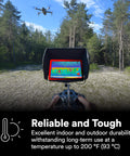 Person operating a drone with thermal imaging monitor in a forest clearing, showing temperature durability up to 200°F (93°C).