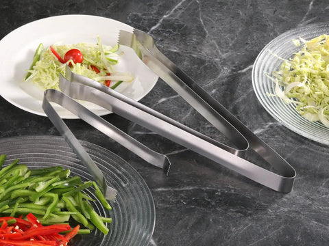 Restaurant Grade 6.5 Inch Pom Tong Set Of 6 Stainless Steel Garnish Tongs with Satin Finish beside sliced vegetables on plates.