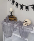 Six Inch Realistic Skeleton Skull Prop With Movable Jaw on draped table with books and candle