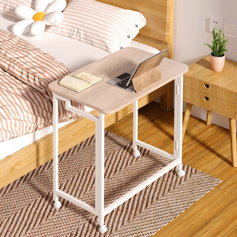 23.6 Inch Mobile Rolling Computer Desk With Wheels Folding Laptop Cart Table in natural and white finish beside a bed.