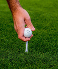 Premium Slick Rubberized Golf Tees With Durable Plastic Base For Low Spin Launch Assorted Colors 4 Pack in use with a golf ball.