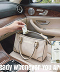 Person placing On The Go Mini Water Activated Towel Tablets in a beige purse on a car seat, showcasing product packaging.