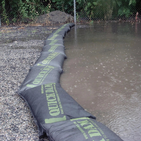 Grab And Go Flood Kit With 20 Water Activated Flood Bags In A Bucket lining a wet ground area for flood control.