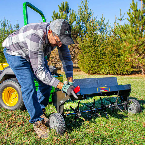 Man using a Tow Behind Plug Aerator With Folding Easy Store Tow Bar, 42 Inch Working Width For Lawn Care, in a grassy lawn.