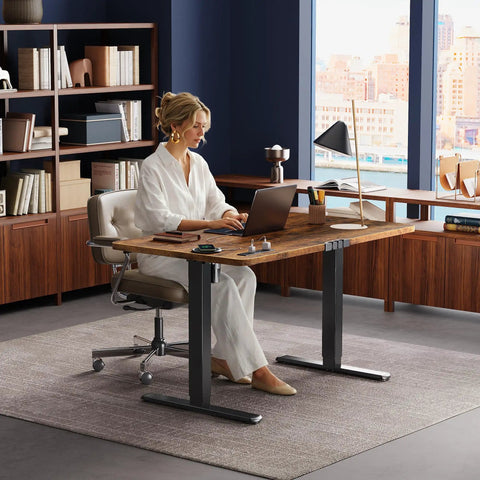 Woman using Huuger 47 X 24 Inch Height Adjustable Electric Standing Desk In Rustic Brown, ergonomic home office setup.