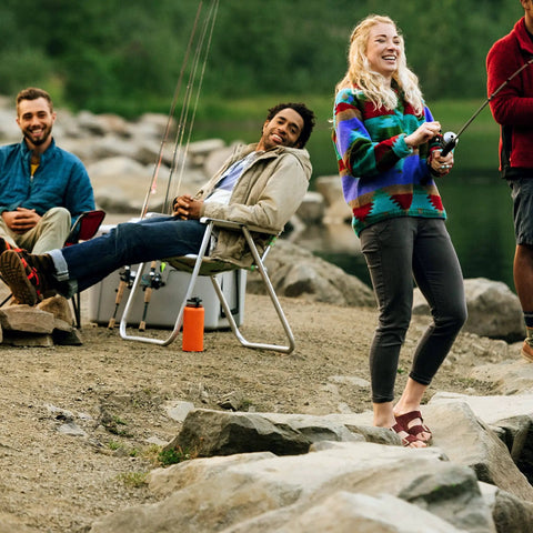 Group of people fishing by a river, one holding a Roam Size 30 Spincast Fishing Reel With Pre Spooled 10 Pound Line Right Or Left Hand Retrieve Built To Last Beefy Stainless Front Cover No Tangle Design Dual Ceramic Pickup Blue.