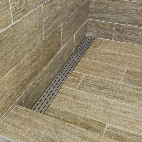 No Fuss Built Tough Brushed Stainless Steel Linear Shower Drain Grate in tiled wet room corner setup.