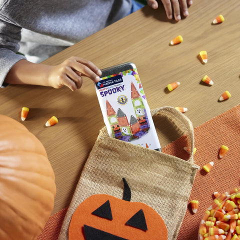 Child holding 24 Piece Halloween Magnetic Building Tiles For Kids To Build A Mini Haunted House, with candies and pumpkin.