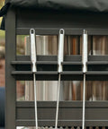 Close-up of black aluminum Station Firewood Rack with UV cover, holding tools and accessories on outdoor shelf.