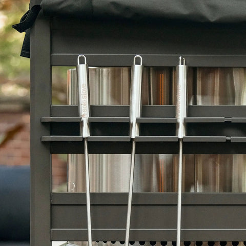 Close-up of black aluminum Station Firewood Rack with UV cover, holding tools and accessories on outdoor shelf.