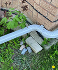 Corner of a brick house with drainage pipe, surrounded by garden plants and stones, hiding stash a spare key in this fake rock that looks like real stone for outdoor gardens and yards geocaching safe key hider type C 1 pack weatherproof discreet outdoor decor.