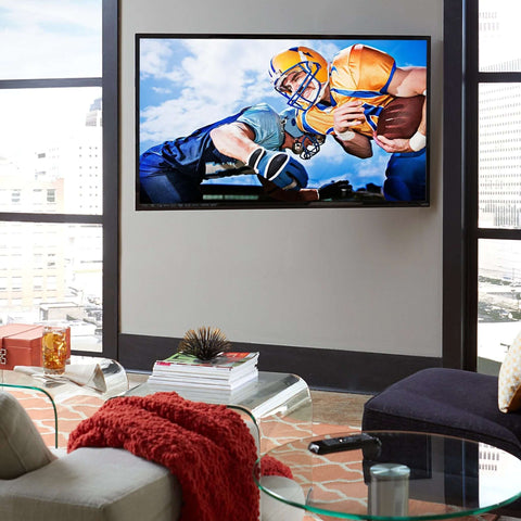 Installed television wall-mount kit; flat-screen TV mounted on beige wall with glass coffee table nearby.