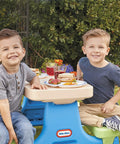 Two boys sitting at a Six Seat Kids Picnic Table With Umbrella Multi Color Outdoor Play Table With Center Cup Holders And Crayon Tray