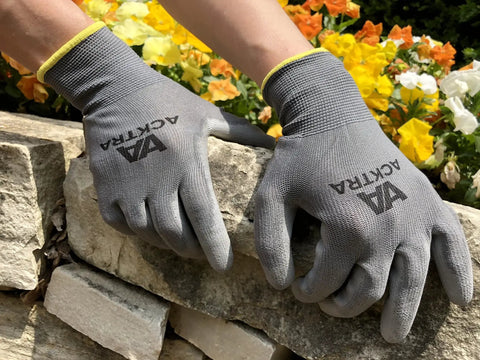 Person wearing gray work gloves, gripping stone blocks, showcasing durability and grip in outdoor setting.