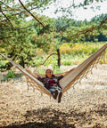 Person relaxing in Heavy Duty Double Hammock With 500 Lb Load Capacity, Tassel Trim, Fishtail Knit Design, cozy outdoor setting