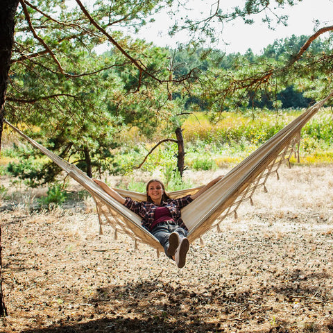 Person relaxing in Heavy Duty Double Hammock With 500 Lb Load Capacity, Tassel Trim, Fishtail Knit Design, cozy outdoor setting
