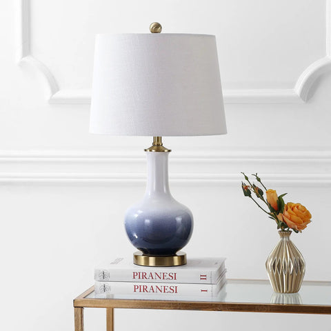 Gradient 25 Inch Ceramic And Brass LED Table Lamp For Bedroom Living Room Office And College Desk Nightstand Accent Light With Included LED Bulb For A Chill Vibe Contemporary Traditional Style In White Navy Finish on glass table.