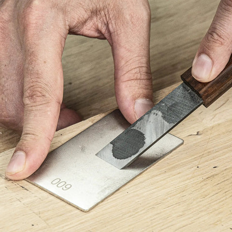 Sharpening a knife with the All In One Credit Card Diamond Sharpening Kit With 180 300 Grit And 600 1000 Grit Stones on wood surface.
