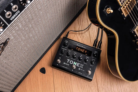 TONEX Pedal Ultra Realistic Stereo Multi-Effects for Guitar and Bass sitting between amplifier and guitar on wood floor.