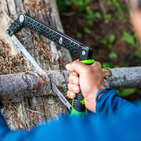 Close-up of folding camp saw with 12-inch blade cutting wood, showcasing flat pocket ready design and bright green accents.