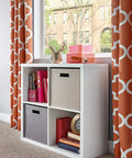 Four Cube Storage Shelf Organizer With Back Panel in home setting, featuring white wood finish, bins, and decor items by window.