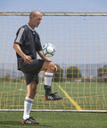 Soccer player practicing near goal wearing Airsport Ankle Brace For Chronic Ankle Instability - Left Medium on synthetic field.