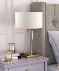 Tall 27 Inch Table Lamp With White Fabric Shade And Seeded Glass Base In Blackened Bronze Finish on a bedroom nightstand
