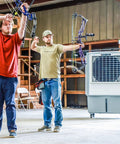 Two men with bows practicing archery in a barn with a Heavy Duty Evaporative Air Cooler With Killer Cooling Power nearby.