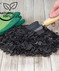 Pile of hardwood charcoal soil additive for indoor plants 2 quarts with small shovel and gloves on wooden surface