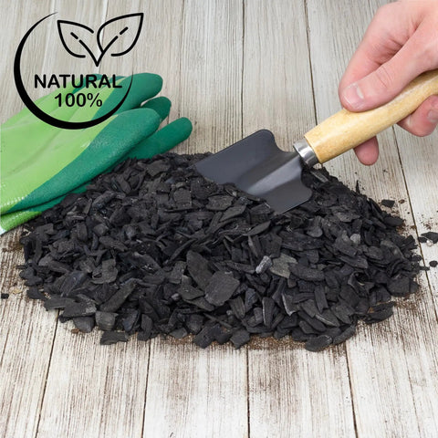 Pile of hardwood charcoal soil additive for indoor plants 2 quarts with small shovel and gloves on wooden surface