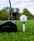Premium Slick Rubberized Golf Tees With Durable Plastic Base For Low Spin Launch Assorted Colors 4 Pack next to a golf driver on grass.