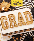 Graduation themed cake with letters 'GRAD' in gold, surrounded by black and gold party decorations.