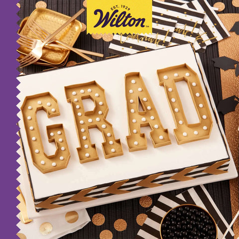 Graduation themed cake with letters 'GRAD' in gold, surrounded by black and gold party decorations.